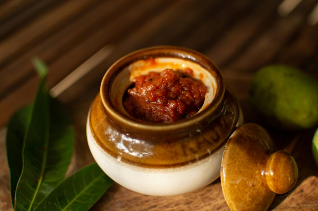 Traditional Indian (aam ka achar recipe) pickle in a rustic ceramic jar on a wooden surface, perfect for food lovers.